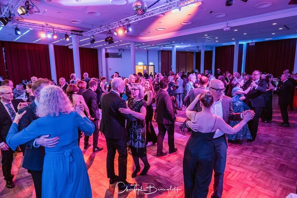 Volle Tanzfläche: Zahlreiche Paare tanzen unter Discokugel und Bühnenlicht in der Stadthalle Mülheim.