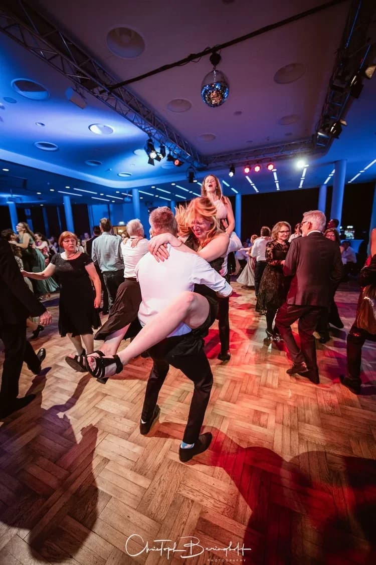 Ein Paar tanzt ausgelassen unter der Discokugel, die Tänzerin springt ihrem Partner lachend in die Arme.